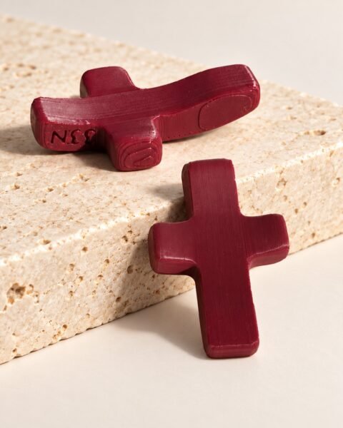 Dos cruces de dedo imantadas burdeos sobre piedra: una tumbada con el grabado 33N en el lateral y otra de pie mostrando la cara lisa