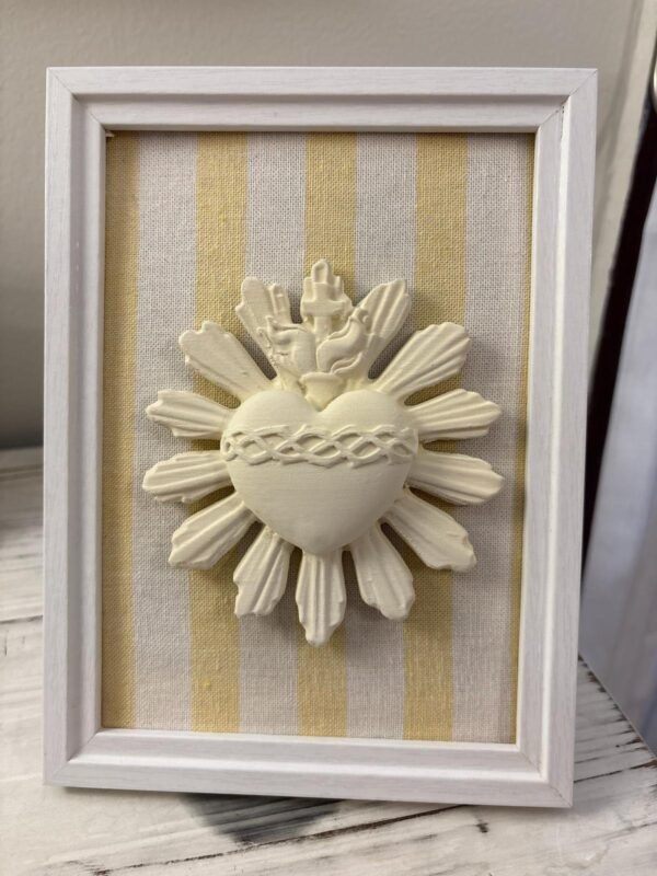 Cuadro del Sagrado Corazón de Jesús en relieve con tela rayas amarillas apoyado de pie sobre un mueble