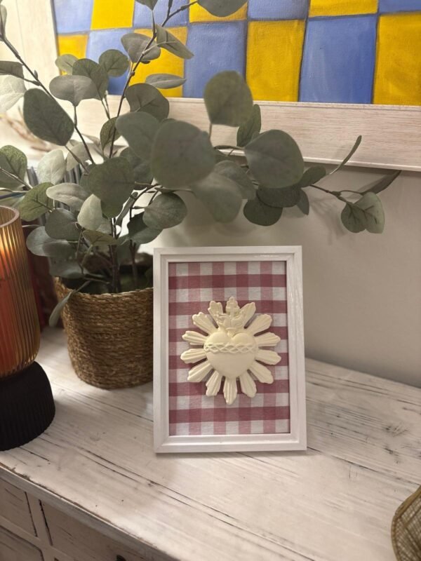 Cuadro del Sagrado Corazón de Jesús en relieve con tela vichy burdeos sobre el mueble del recibidor