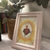 Detente del Sagrado Corazón de Jesús con marco madera clara sobre el mueble del recibidor